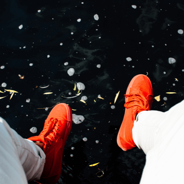 Pernas com tênis laranja acima de um rio